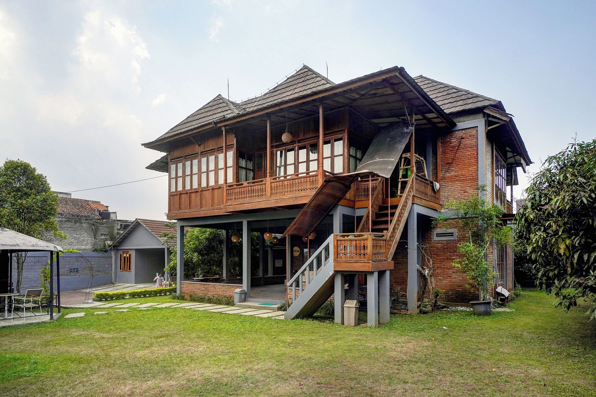 Una casa de madera de dos pisos con un balcón, una escalera y un pequeño jardín.