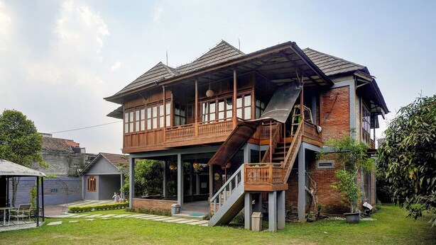 Een houten huis met twee verdiepingen, een balkon, een trap en een kleine tuin.