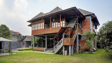 Una casa de madera de dos pisos con un balcón, una escalera y un pequeño jardín.