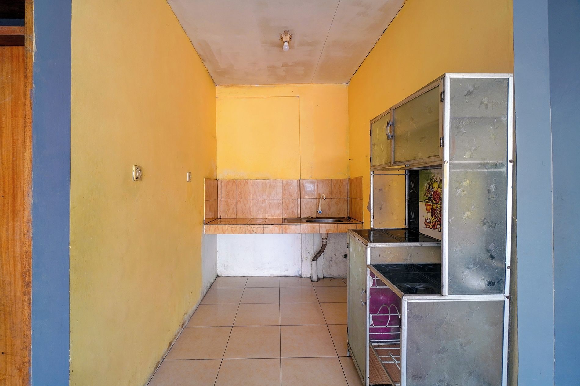 A narrow hallway with a kitchen area featuring a sink, cabinets, and a tiled floor.