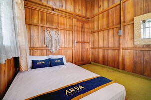 A wooden-paneled room with a bed, two pillows, a macrame wall hanging, and a window with a curtain.