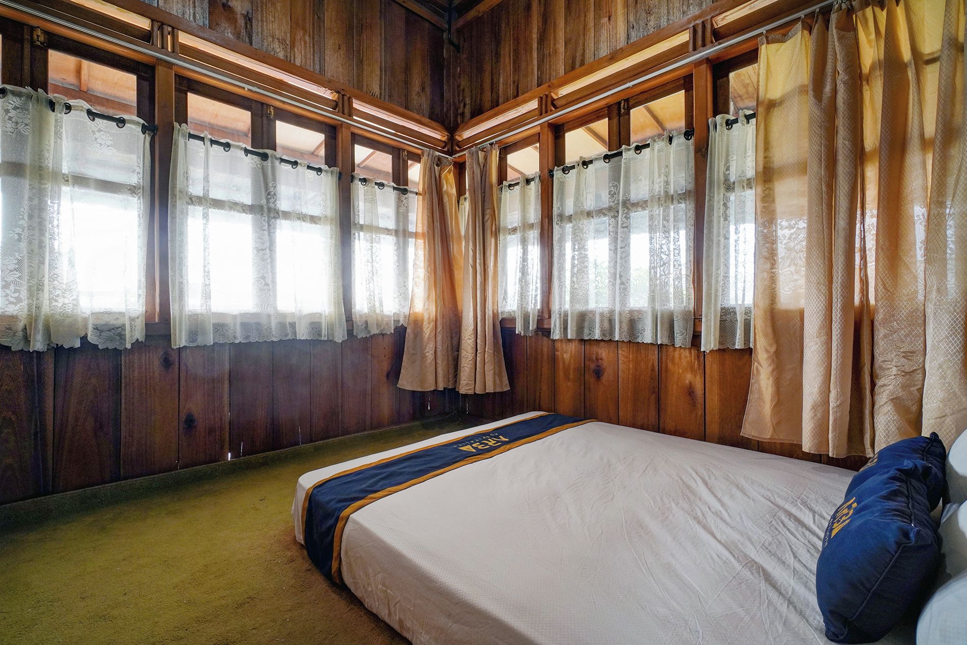 Une pièce avec un lit, des murs en bois et des fenêtres avec des rideaux.