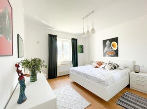 Un dormitorio moderno con una cama grande, mesitas de noche, un escritorio y una ventana con cortinas.