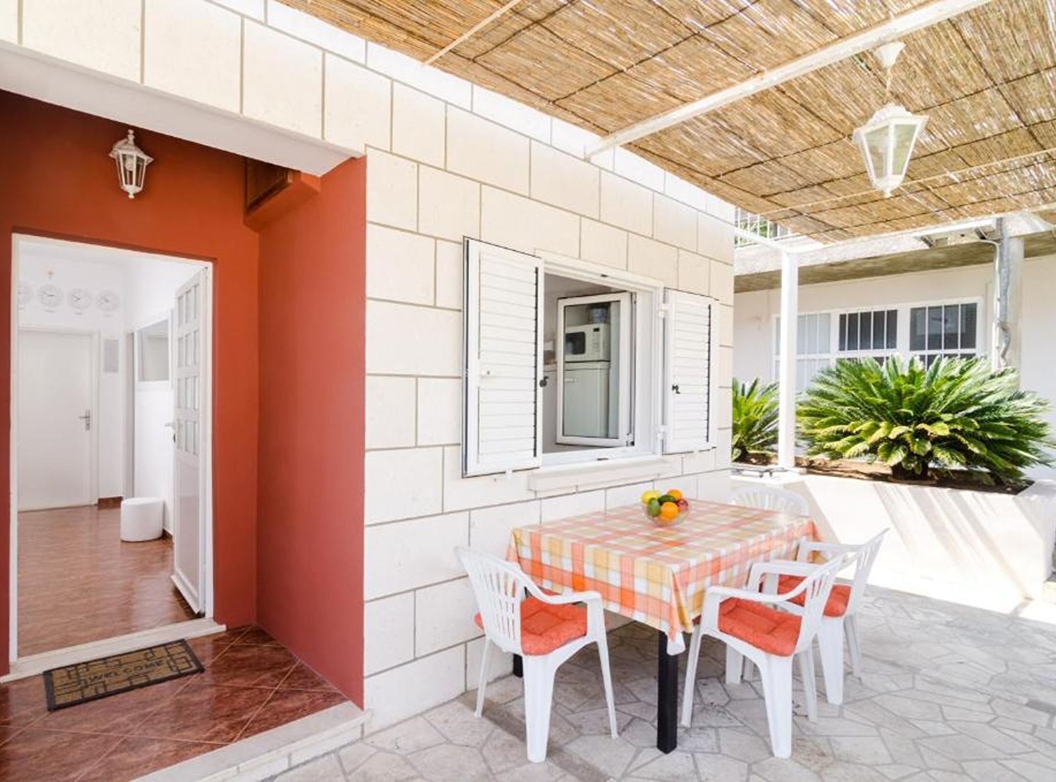 Un patio cubierto con una mesa y sillas, una puerta que da a una habitación interior y una ventana con persianas.