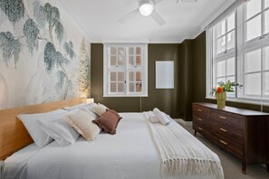 Ein Schlafzimmer mit Bett, Schminktisch, Fenster und Deckenventilator.