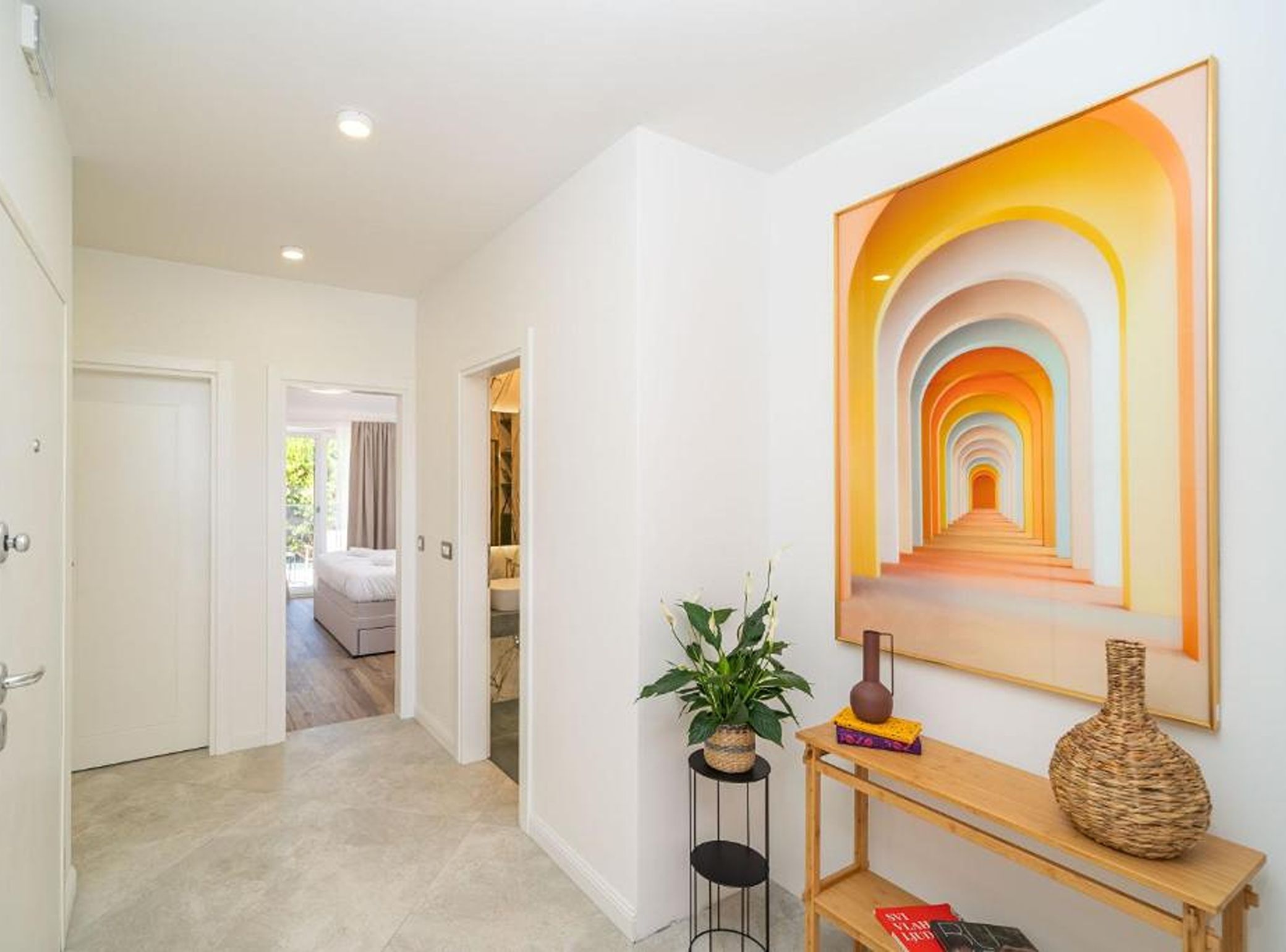 A hallway with a modern art piece, a potted plant, and a console table with books and a vase.