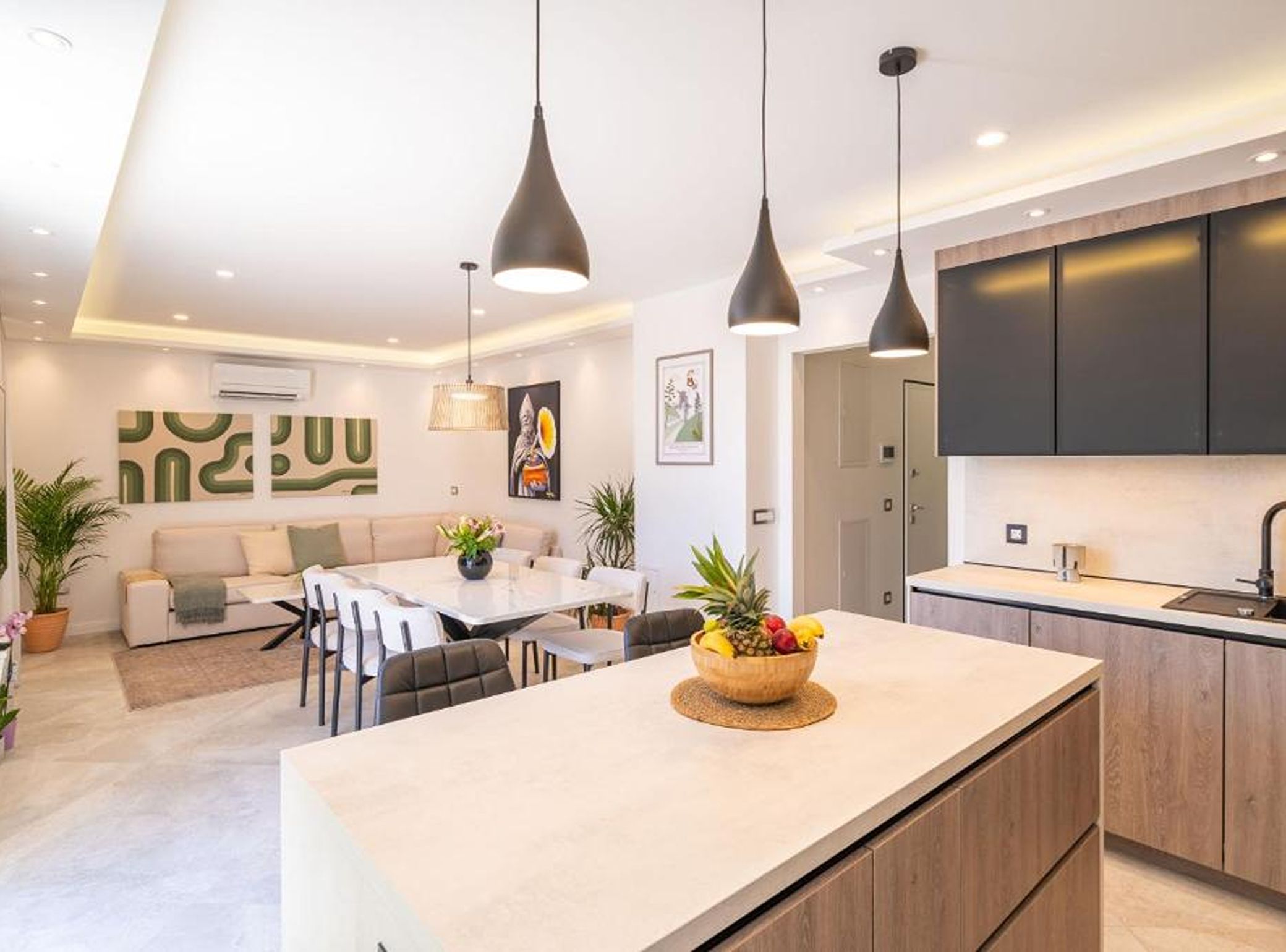 A modern kitchen with a central island, pendant lighting, and a dining area with a sofa and chairs.