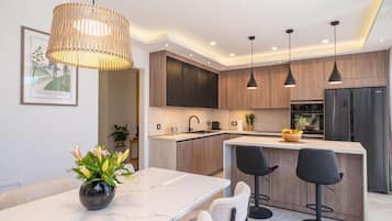 Eine moderne Küche mit Holzausbau, einer Mittelinsel, Pendelleuchten und einem Essbereich mit einem Blumenstrauß.