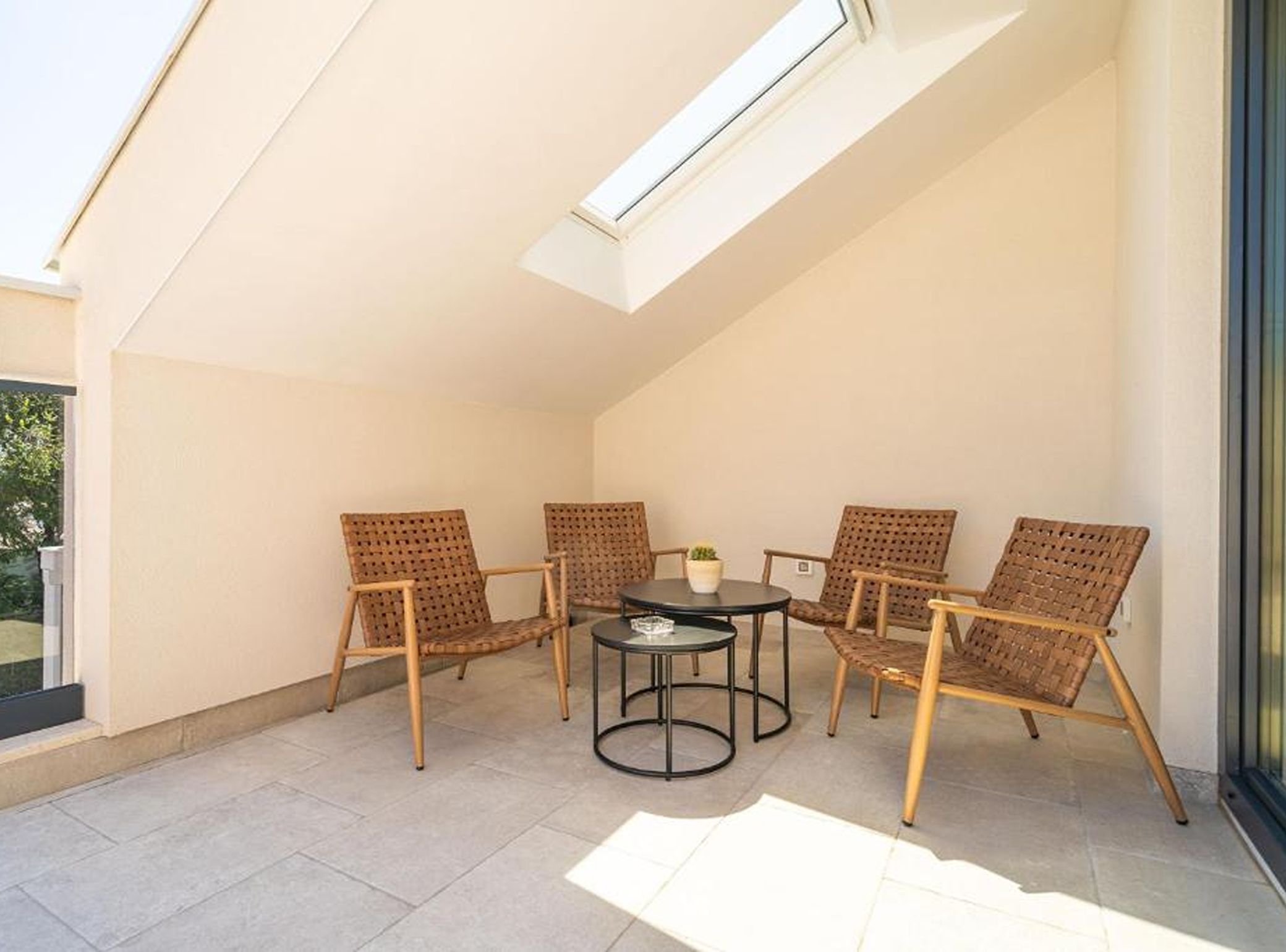 A sunlit patio with a table and four wicker chairs, a small potted plant, and a skylight.
