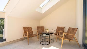 Une terrasse ensoleillée avec une table et quatre chaises en osier, une petite plante en pot et une lucarne.