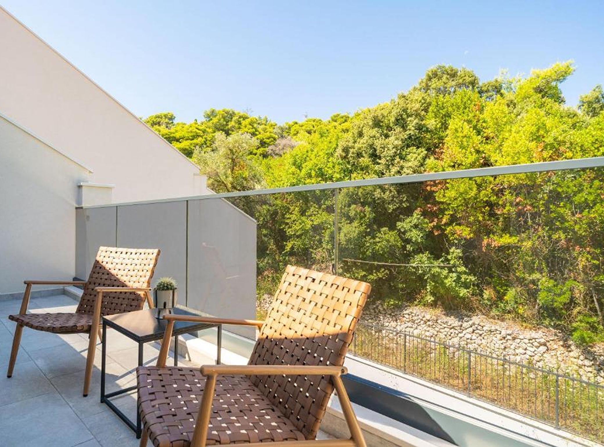 A balcony with two wicker chairs and a small table, overlooking a lush green landscape.