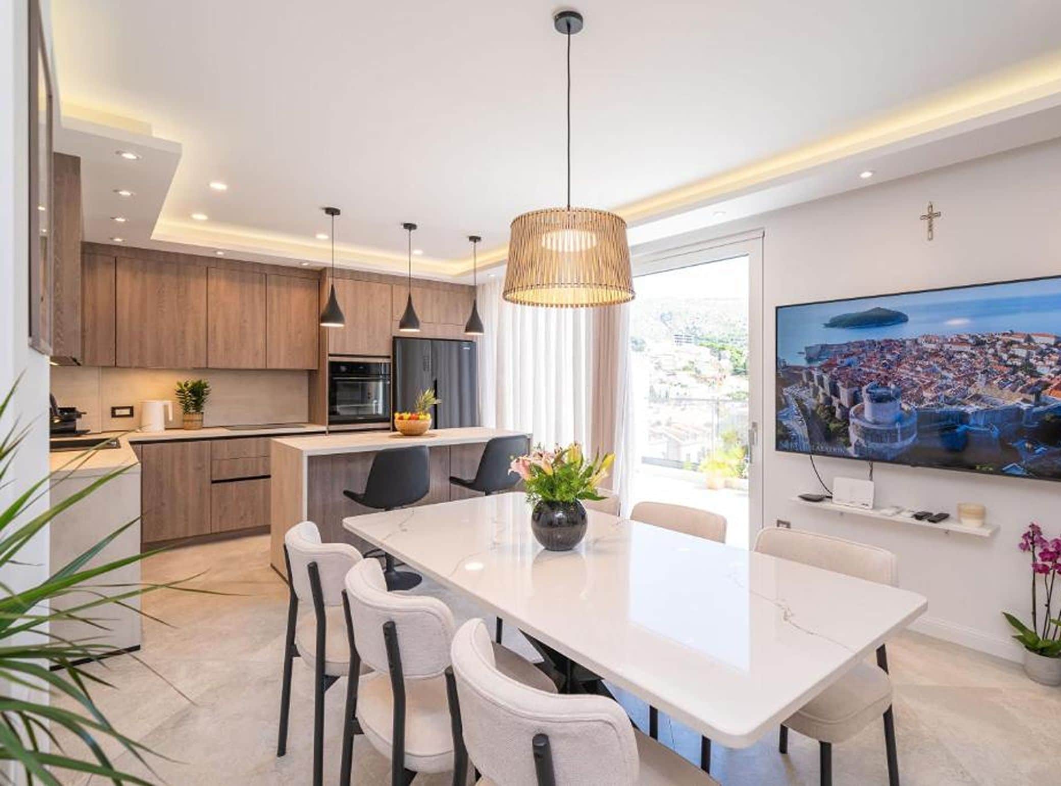 A modern kitchen with wooden cabinets, a central island, and a dining area with a large TV.