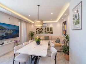 A modern living room with a dining area, featuring a large flat-screen TV, a sofa, a coffee table, and a chandelier. - Luxumbra Penthouse Apartment (Dubrovnik)
