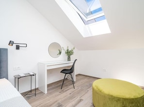 A modern loft bedroom with a skylight, a white desk, a black chair, and a green ottoman. - Luxumbra Penthouse Apartment (Dubrovnik)