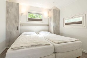 Une chambre à coucher avec un lit, deux fenêtres et une armoire.