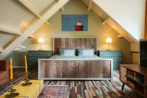 A bedroom with a sloped ceiling, a wooden bed, two bedside tables with lamps, a painting of a lighthouse, and a patterned rug. - Ouddorp Vakantiehuisje Zon en Zee (OUDDORP ZH)