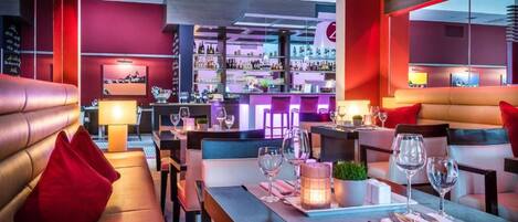 A restaurant with a bar area, seating with red cushions, and a well-lit ambiance.
