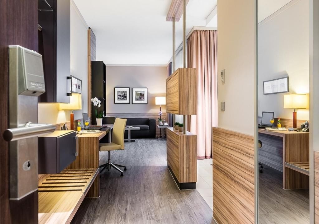 Ein Hotelzimmer mit einer Küchenzeile, einem Schreibtisch, einem Sofa und einem Spiegel.