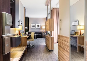 A hotel room with a kitchenette, a desk, a sofa, and a mirror.