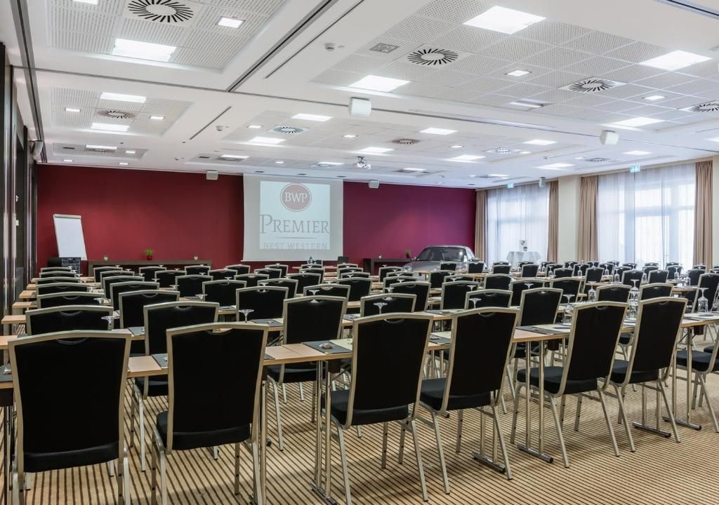 Ein Konferenzraum mit Tischen und Stühlen, einer Projektionsleinwand mit dem Text 'BWP Premier' und einer roten Akzentwand.