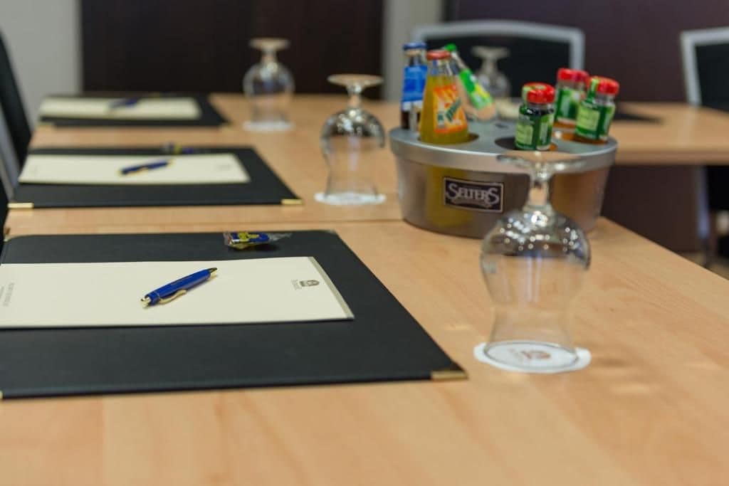 Una mesa de conferencias con documentos, bolígrafos, una botella de agua y un vaso.