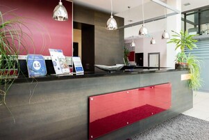 Una recepción con un detalle rojo, una lámpara colgante moderna y una planta en maceta.
