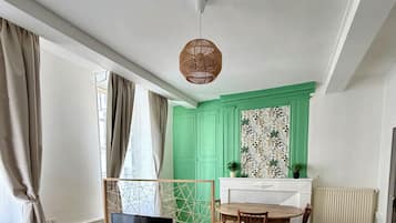 Een kamer met een televisie op een houten standaard, een eettafel met stoelen, een kamer met een patroon op de muur en een radiator.
