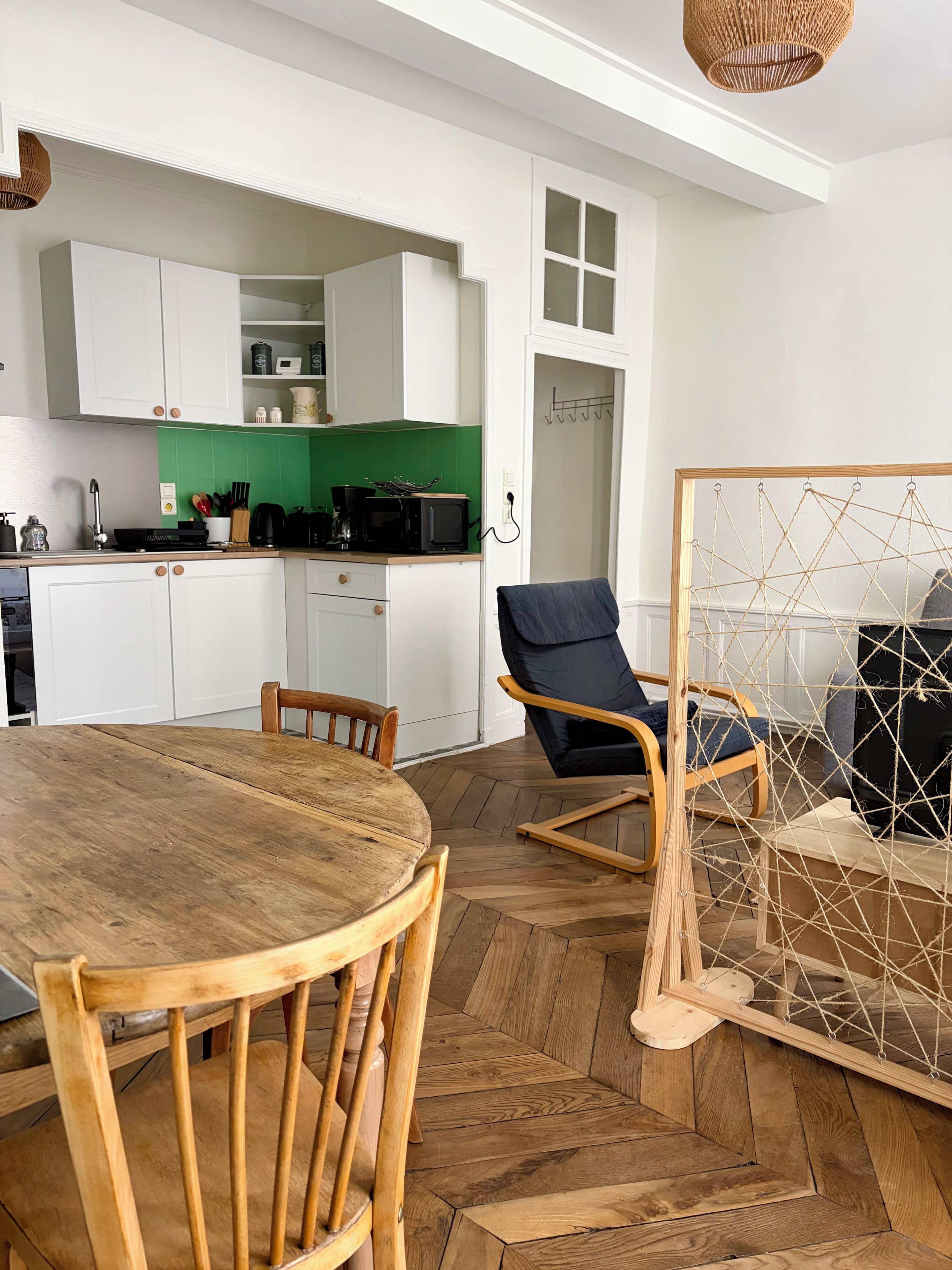 Uma cozinha moderna com armários brancos, painel de fundo verde e um espaço de refeições com mesa e cadeiras de madeira.