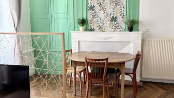 Een eethoek met een houten tafel en stoelen, een witte open haard en een groene wand met een bloemmotief.