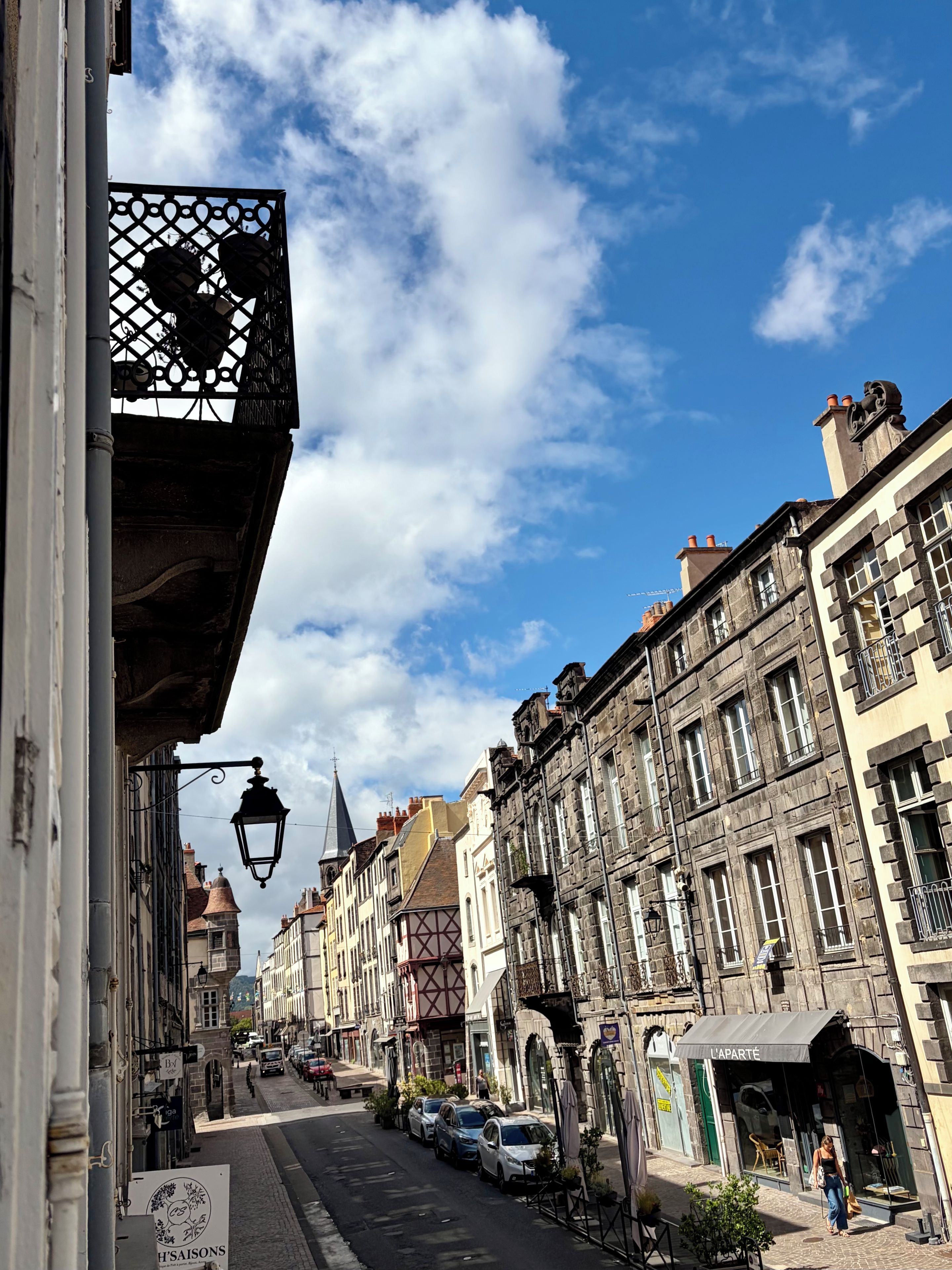 A street with historic buildings, a clear sky, and parked cars.