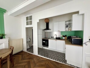 A compact kitchen with white cabinetry, a black stove, and a green backsplash. - L'émeraude - Charming Apartment in Riom (Riom)