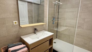 Een moderne badkamer met een douchecabine van glas, een grote spiegel en een houten wastafelmeubel.