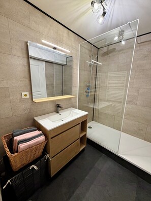 A modern bathroom with a glass-enclosed shower, a large mirror, and a wooden vanity. - L'émeraude - Charming Apartment in Riom (Riom)