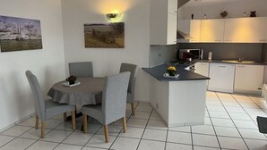 Uma cozinha moderna com armários brancos, uma área de jantar com cadeiras cinzas e obras de arte nas paredes.