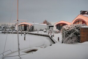 Ett snötäckt utomhusområde med en brygga, en byggnad med ett välvt tak och en snötäckt buske.