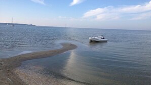 Mar calmo com um barco perto da costa, uma praia de areia e céu claro.