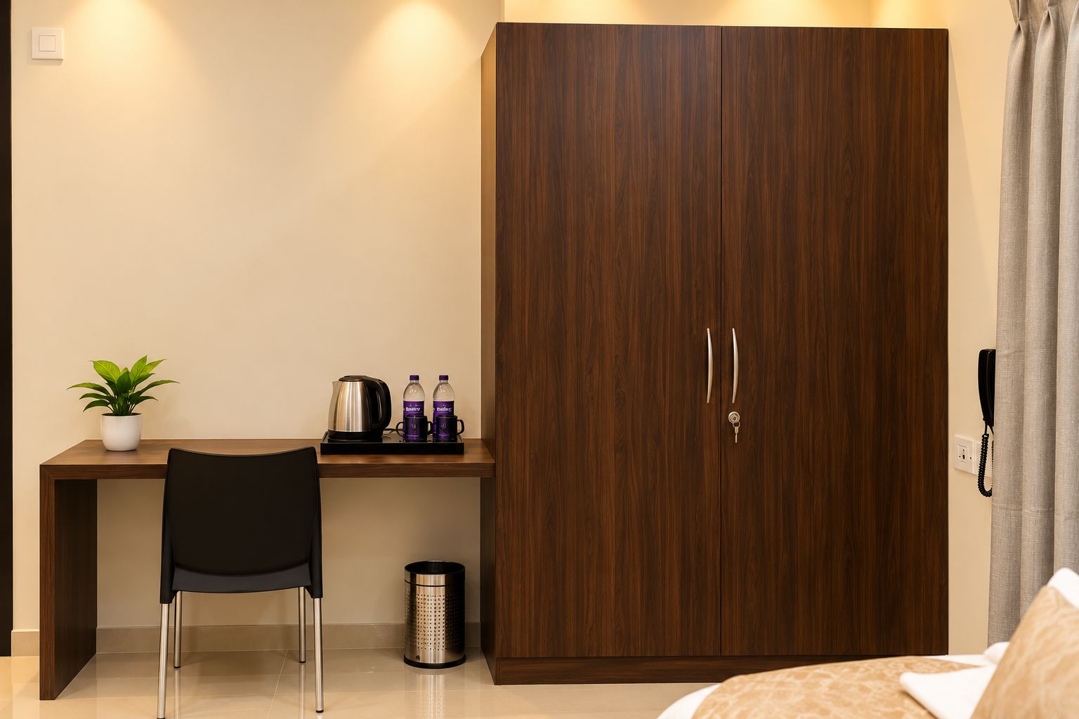 Habitación de hotel con un armario de madera, un escritorio con una silla, una planta en maceta, un hervidor y dos botellas.
