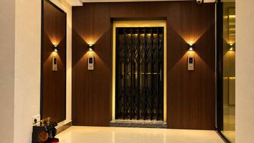 A modern elevator entrance with a digital display, wall-mounted lighting, and a polished marble floor.