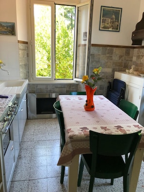A kitchen with a dining table, chairs, a stove, and a window with a view of greenery. - Vrbo Property (Liguria)