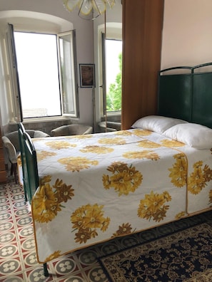 A bedroom with a bed, a chair, a window, and a patterned floor. - Vrbo Property (Liguria)