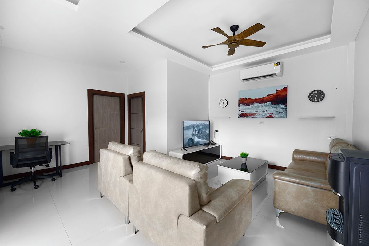 A modern living room with a sofa, a television, a desk with a computer, and a ceiling fan.