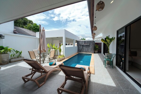 A modern outdoor pool area with lounge chairs, a small table, and potted plants. - Elyana Villa -3BR Oasis in Rawai (Tambon Rawai)