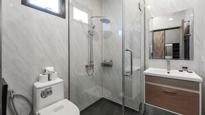 Een moderne badkamer met een douche met glazen wand, een toilet, een wastafel en een spiegel.