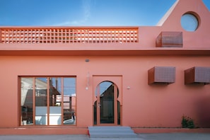A building with a pink facade, large windows, and a small entrance.
