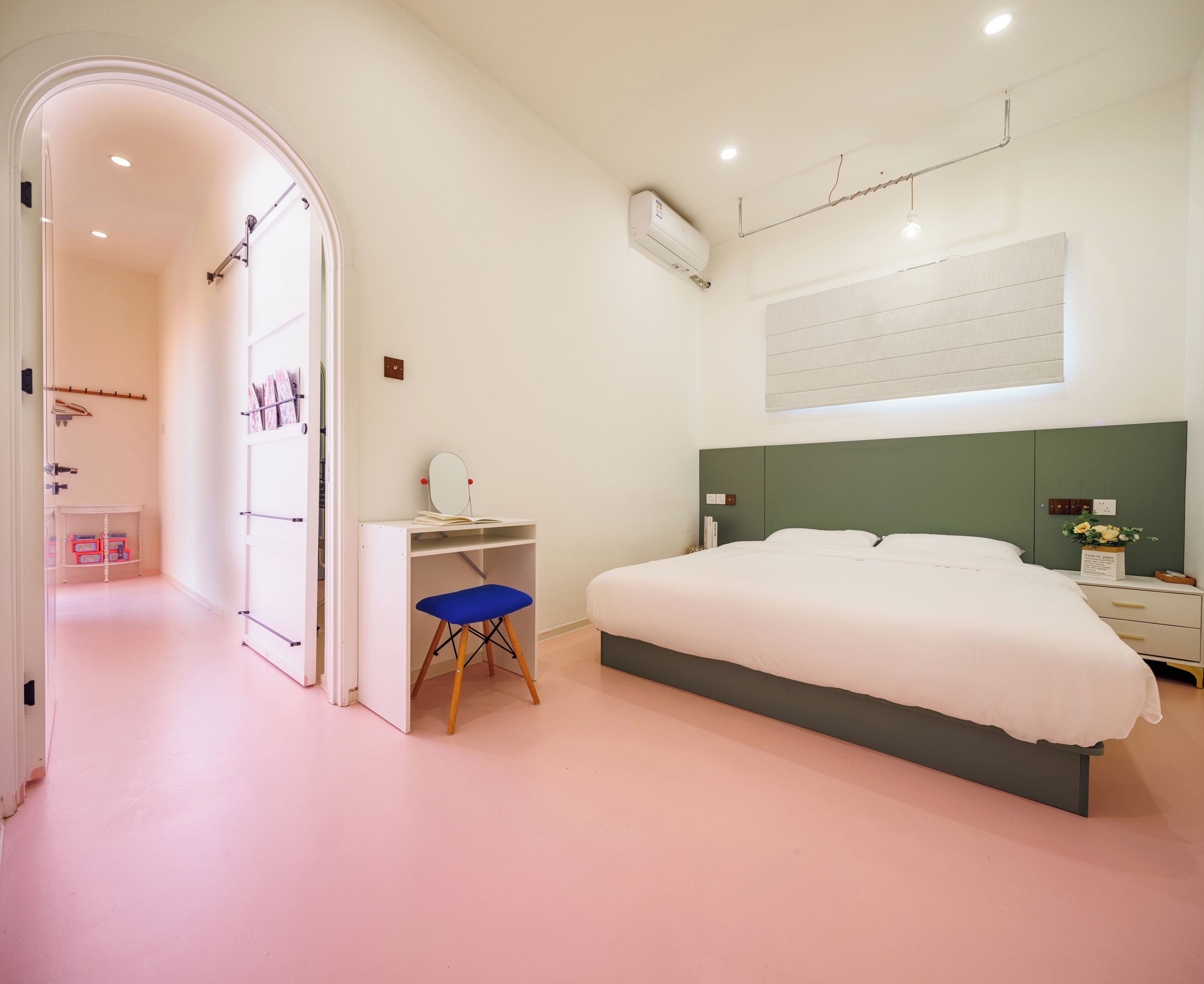 A bedroom with a bed, a desk, and a chair. There is a wardrobe with a mirror and a shelf with books.