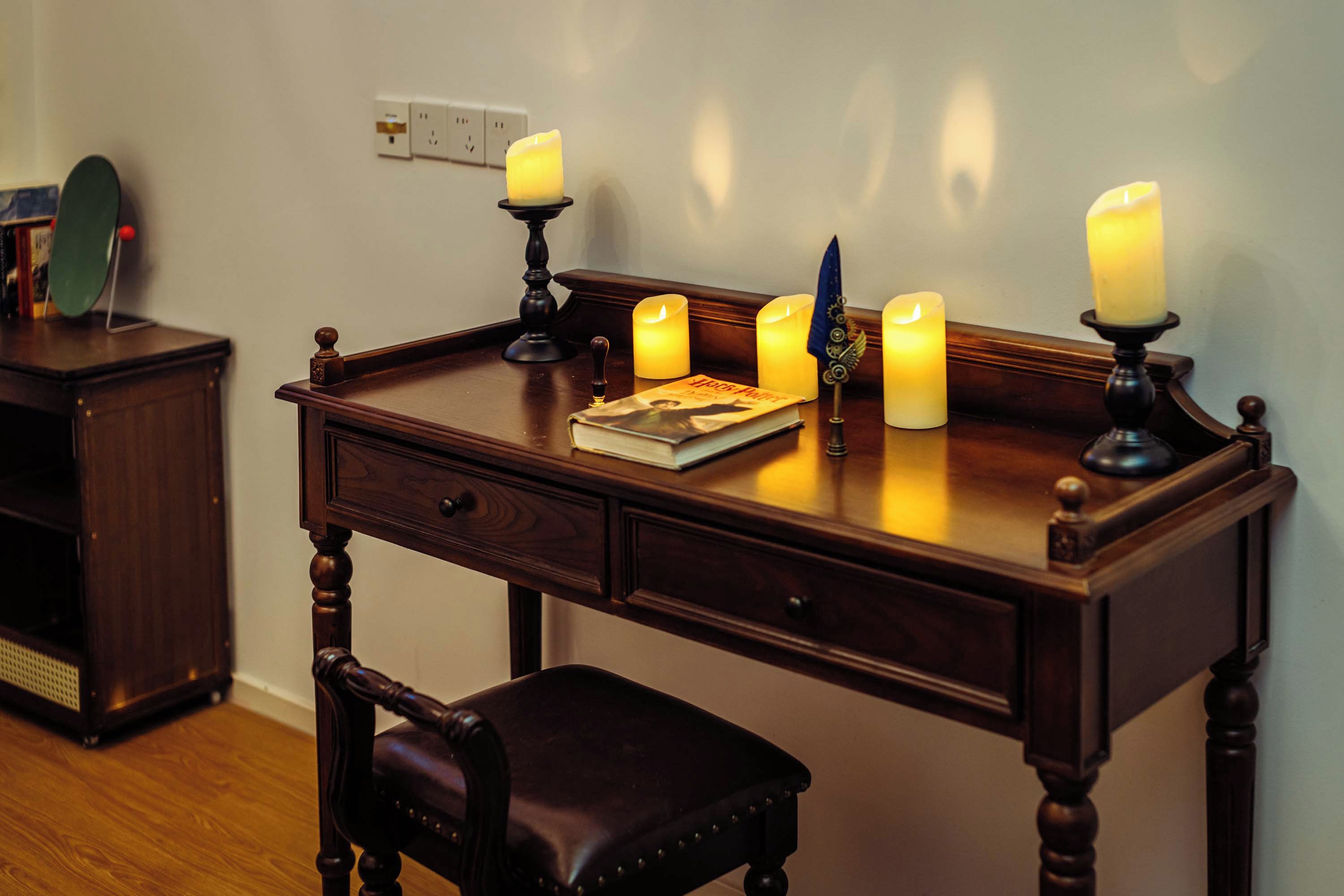 Un escritorio de madera con cuatro velas encendidas, un libro y una pluma.