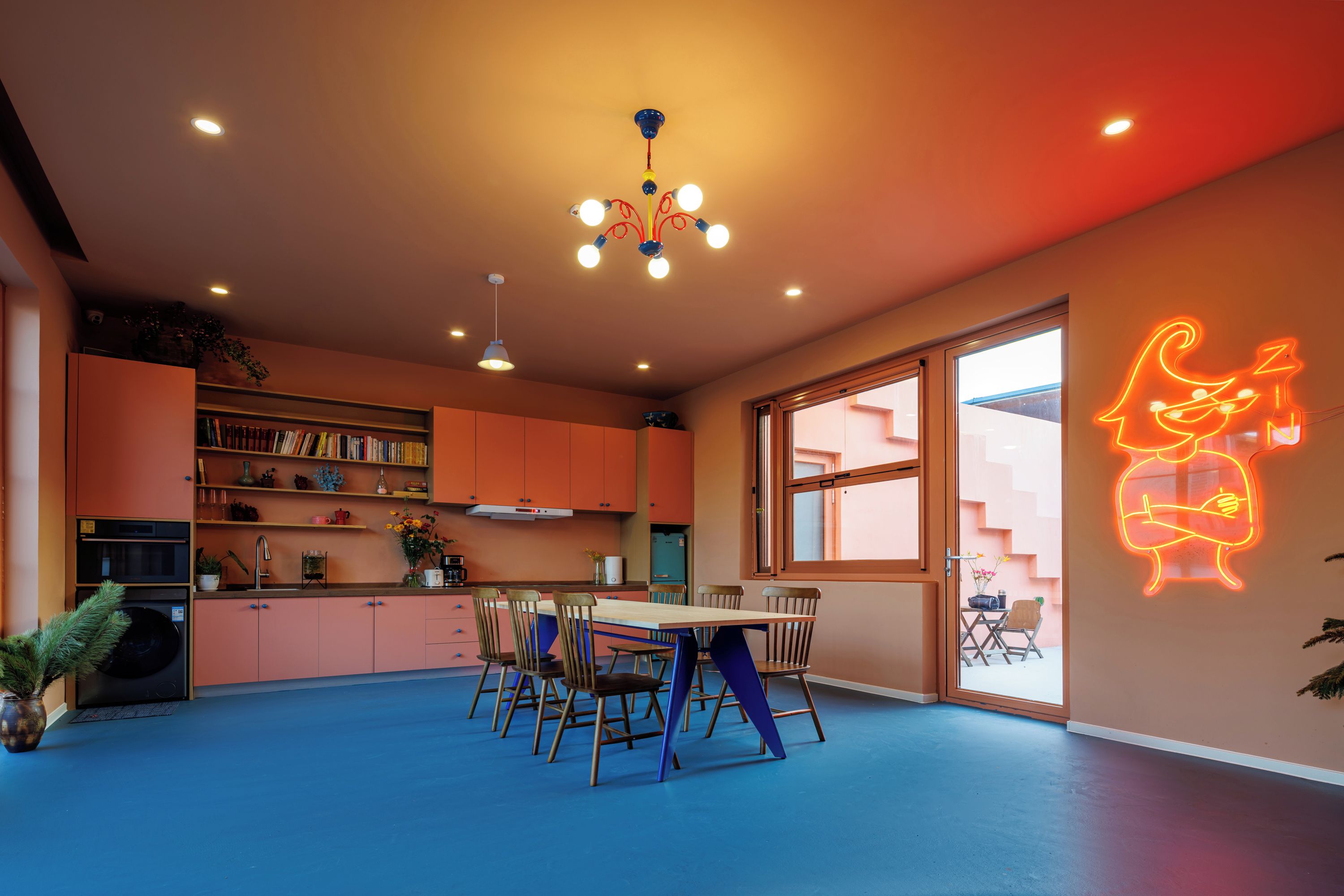 A modern kitchen with a dining area, featuring a neon sign, a large window, and a blue floor.