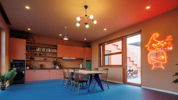 A modern kitchen with a dining area, featuring a neon sign, a large window, and a blue floor.
