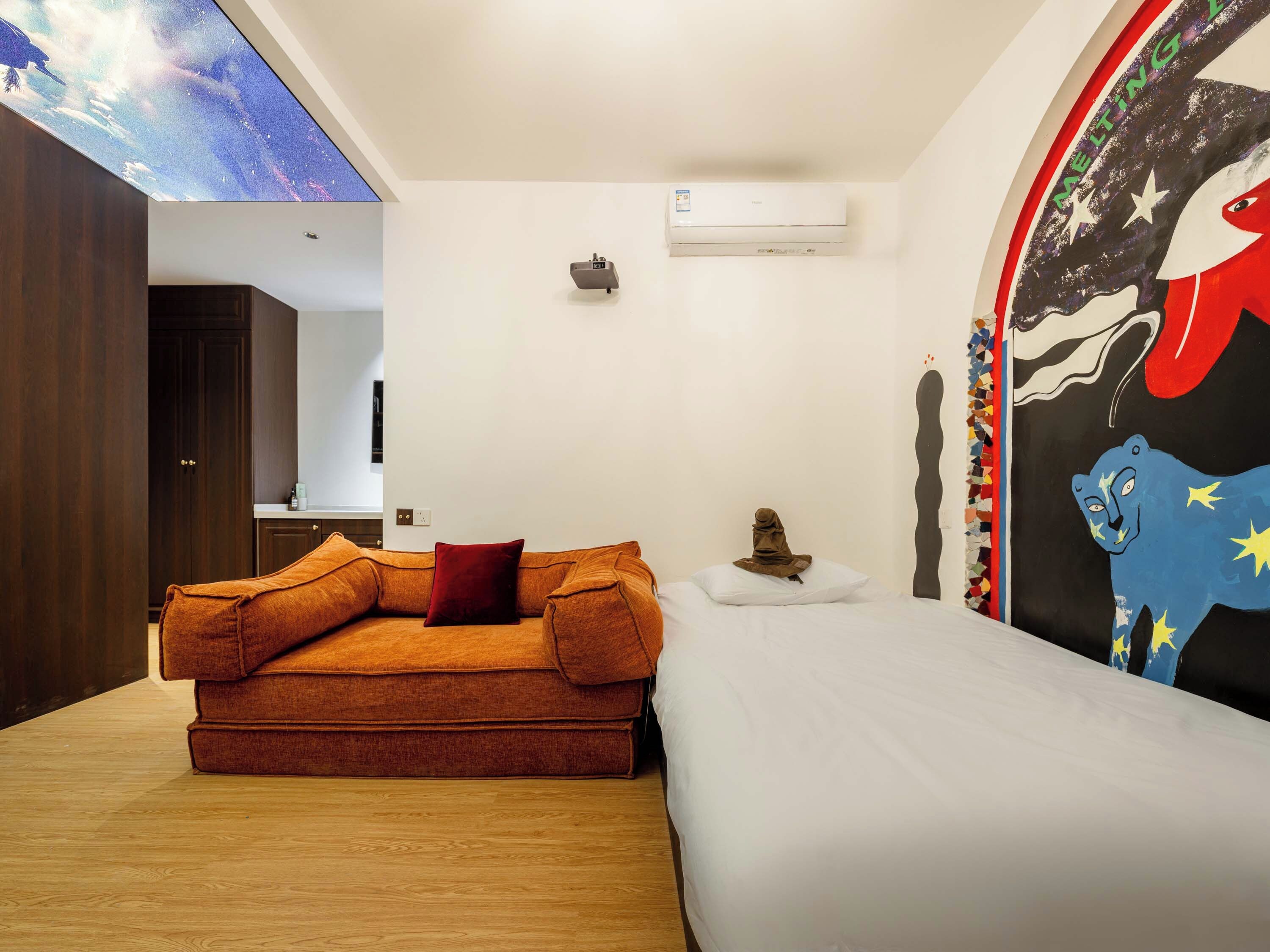 Ein Zimmer mit einer Couch, einem Bett, einem Deckenprojektor, einer Klimaanlage und einer Wand mit einer Grafik.