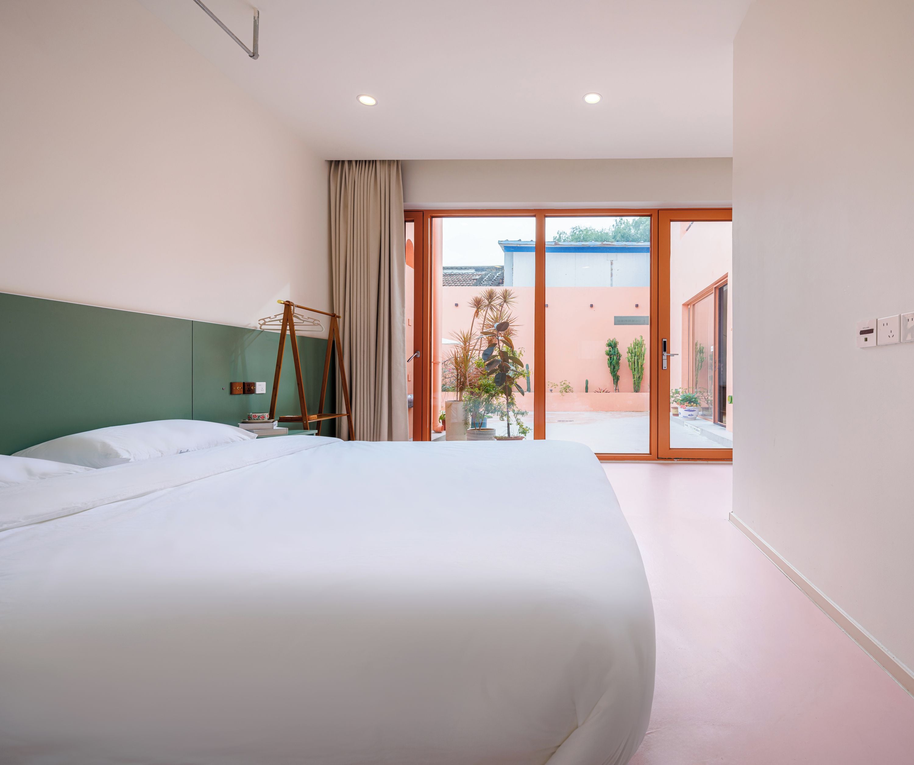 A hotel room with a large bed, a wooden hanger, a window with curtains, and a view of the outside.